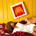 Vol IV The Doll Wall framed art print - golden lady silk print in white frame styled with woman and cat on rose petal backdrop yellow wall
