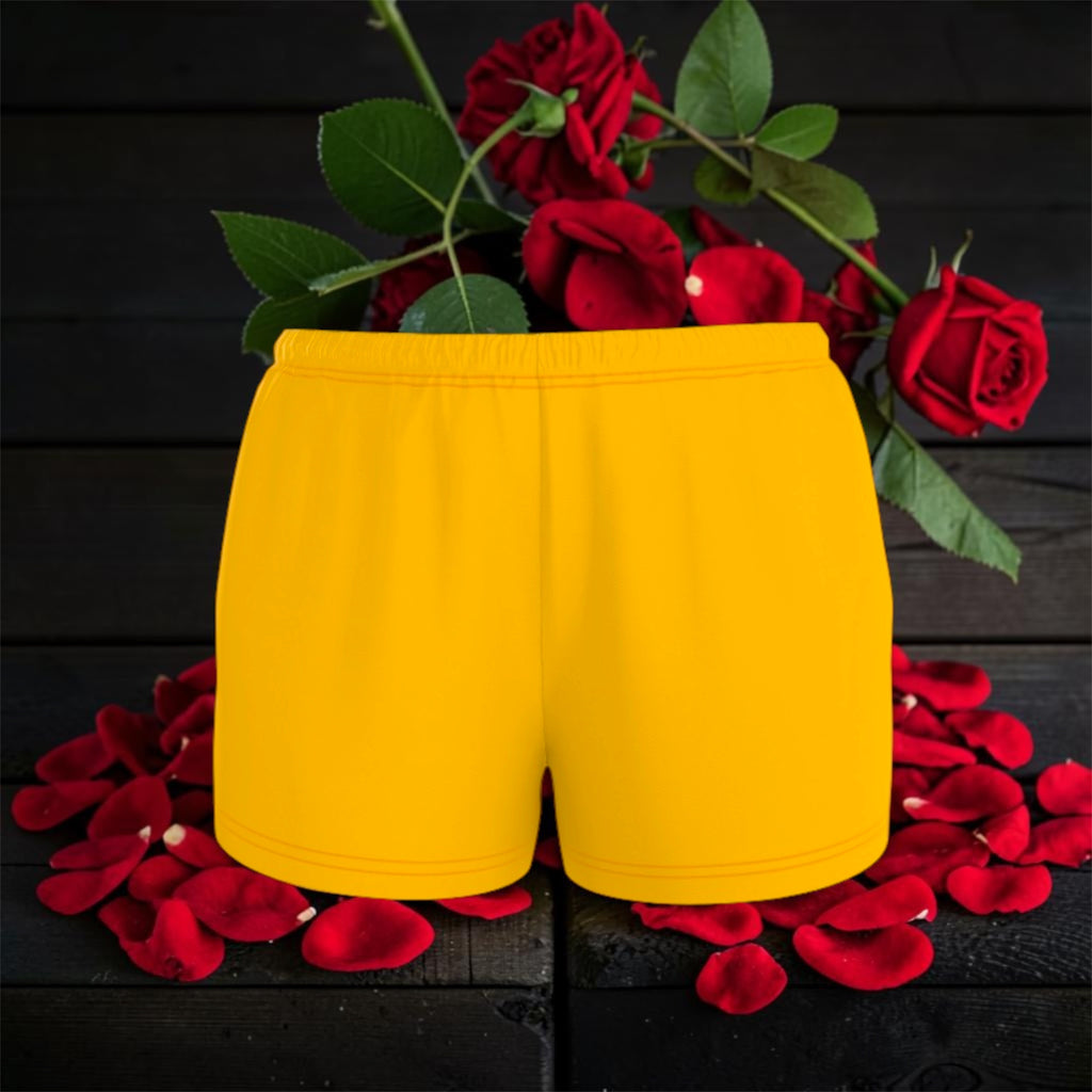 Image 1 — Front flat lay (dark backdrop, red roses): Golden Expression Art Vol IV The Golden Ease Short — golden yellow organic cotton relaxed shorts with elastic waistband, front view, rose petal editorial backdrop