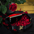 Image 1 (open interior): Vol IV — The Golden Riot Fanny Pack — open top-down view showing scarlet red interior lining with gold zipper, black body with gold buckle clasp, rose petal fill inside, golden yellow wood wall editorial backdrop — Golden Expression Art