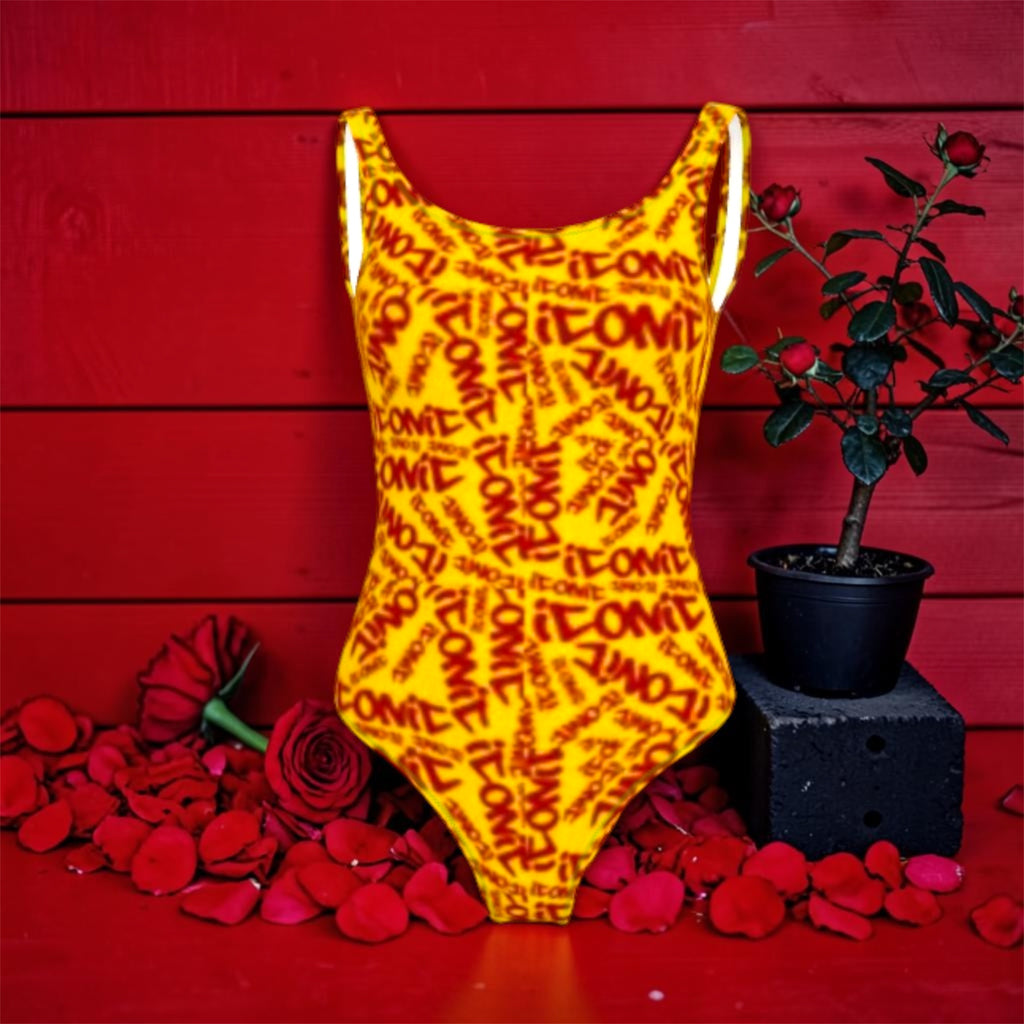 Image 2 — Front full view (scarlet red wall, rose petals): Golden Expression Art Vol IV The ICONIC One-Piece — golden yellow ICONIC all-over print one-piece, scoop neck and spaghetti straps, scarlet red wall backdrop with red roses