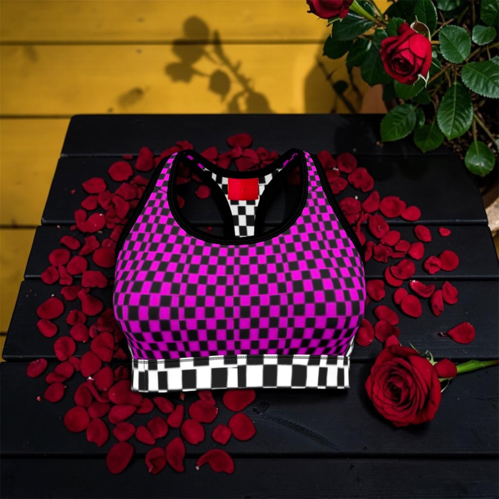 Image 1 (front flat lay, single bra): Vol IV — The Magenta Checkmate Bra Top — magenta and black checkered racerback sports bra with black and white checkered hem band, rose petal editorial backdrop, Stay Golden Edit
