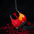 Image 1 (front, hanging on chain, dark backdrop): Vol IV — The Queen Dolly Sports Bra — front view suspended on chain, scarlet red body with Doll Wall golden hair art print, black & white checkered straps and underband, black trim, rose petal dark editorial backdrop — Golden Expression Art 