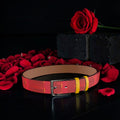 Image 1 — Front view (dark backdrop, rose petals): Golden Expression Art Vol IV The Scarlet Flame Belt — scarlet red bubble napper leather belt with gold keeper loop and gunmetal pin buckle, rose petal editorial backdrop