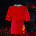 Image 1 — Front view (dark backdrop, rose petals): Golden Expression Art Vol IV The Scarlet Rule Tee — scarlet red oversized tee with black and white checkered collar detail, Doll Wall graphic at hem, rose petal editorial backdrop