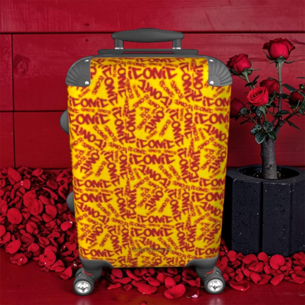 The ICONIC Getaway carry-on luggage — front view, all-over ICONIC print in golden yellow and scarlet red, spinner wheels, red wall backdrop