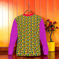 Vol II — The Garden of Paradise Sweatshirt, front view, all-over Eden repeat print, animated woman golden yellow base blue and green tones, solid magenta fuchsia sleeves, red ribbed collar, GEA