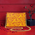 The ICONIC Soirée — front view, textured bubble leather clutch with ICONIC all-over print in golden yellow and scarlet red, gold chain strap, rose petal editorial backdrop