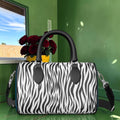 The Zebra Bloom Duffle Bag showing the black and white zebra print side with black leather top handles and adjustable webbing shoulder strap, in front of red roses