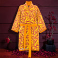 The Decree Kimono Wrap — front view, golden yellow silk with all-over scarlet red ICONIC lettering, self-tie golden sash, rose petal editorial