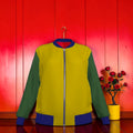 Vol II — The Eden Color-Block Denim Jacket, front view, golden yellow body, forest green sleeves, royal blue ribbed collar with red interior flash, white zip closure, royal blue ribbed cuffs and hem, GEA