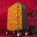 The ICONIC Getaway carry-on luggage — side angle view, all-over ICONIC print in golden yellow and scarlet red, matte black hardware, rose petal backdrop