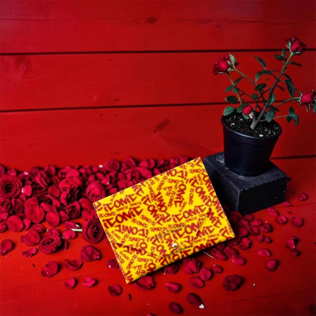 The ICONIC Envelope Card Holder — wallet detail shot, ICONIC all-over print, rose petal backdrop