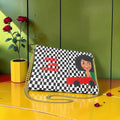 Iconic Signature Clutch Bag - front view, black and white checkered print with ICONIC doll graphic and Bold And Iconic red text, gold chain strap