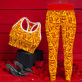 The ICONIC Flex Yoga Pant — set shot with ICONIC sports bra, golden yellow ICONIC all-over print with scarlet red lettering and red waistband, styled with black heels on rose petal backdrop