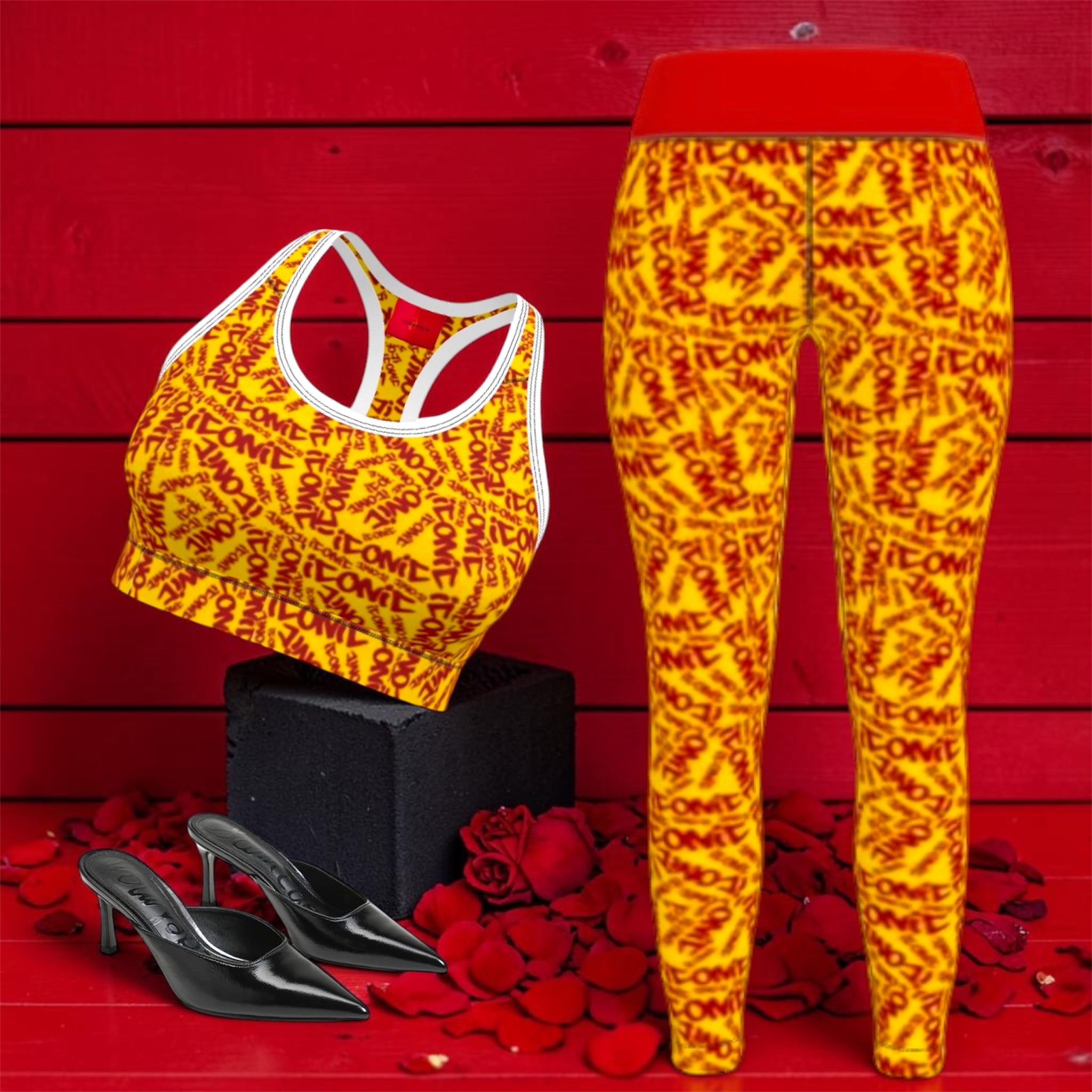 The ICONIC Flex Yoga Pant — set shot with ICONIC sports bra, golden yellow ICONIC all-over print with scarlet red lettering and red waistband, styled with black heels on rose petal backdrop