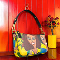 Vol II — The Eden Doll Baguette — front view featuring all-over Doll Wall print with GEA figures on golden yellow body, black leather top handle, gold hardware, structured baguette silhouette, Golden Expression Art