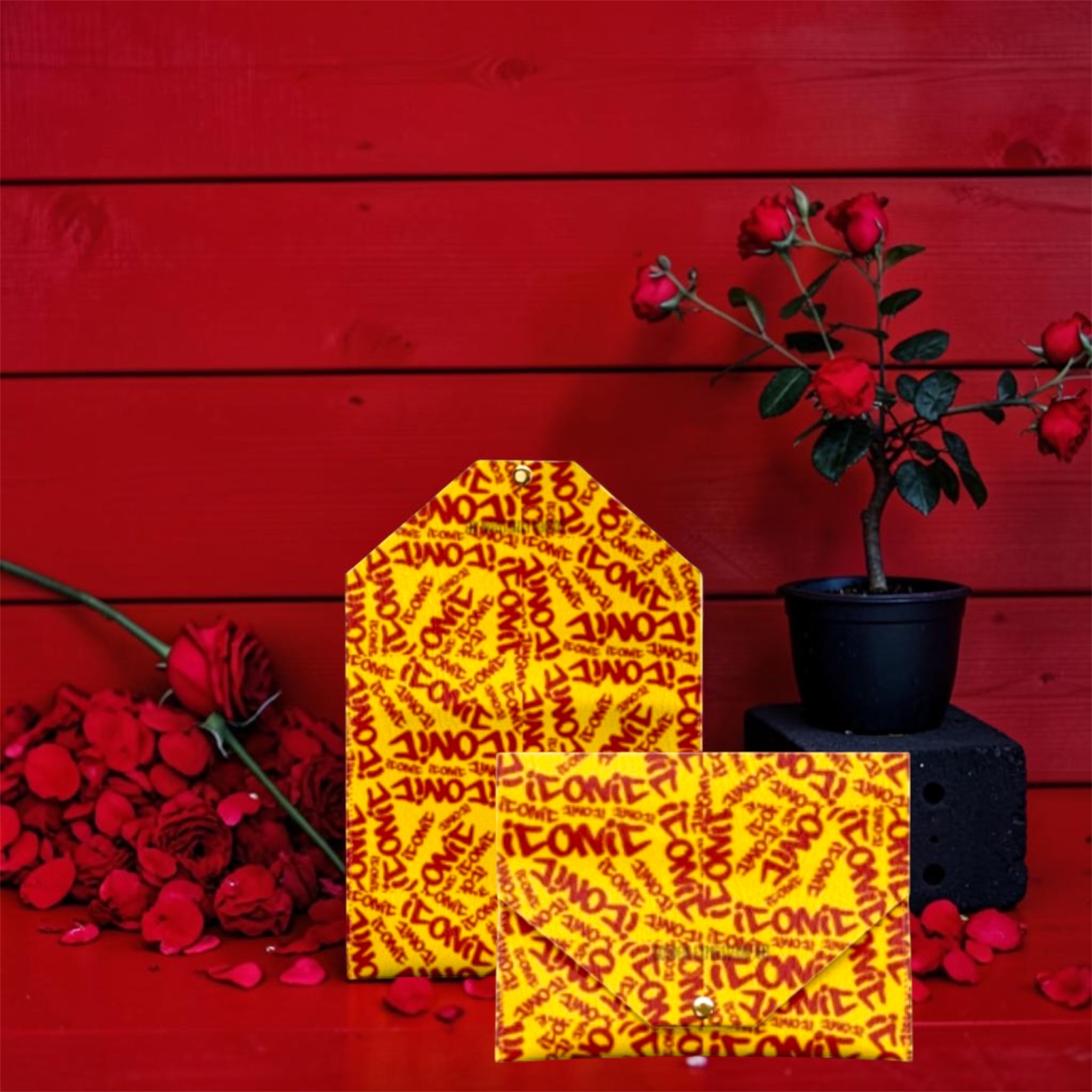 The ICONIC Envelope Card Holder — full envelope silhouette closed, ICONIC all-over print, red wall editorial with rose petals